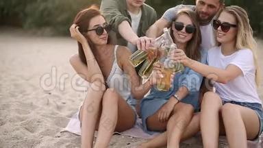 一群朋友在日落时分在海滩上玩着享受饮料和放松的乐趣。 男女青年